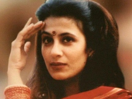 Image of Jessica Lal with long dark hair and bindi, wearing a red patterned saree, gazes thoughtfully, hand raised to her forehead. The tone is reflective and serene.