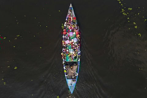 Aerial view of a crowded blue boat on dark water, filled with people in colorful clothing, conveying a sense of community and vibrant energy.