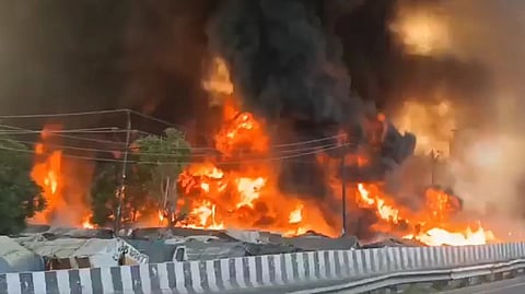 Thick black smoke rising over a densely packed slum area in Lucknow as flames engulf rows of shanties during a massive fire incident.