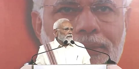In the image PM Modi is shown adressing the public wearing white 