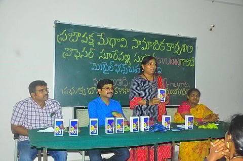 Sujatha Surepally with three others standing in front of a blackboard, behind a table with smartphones
