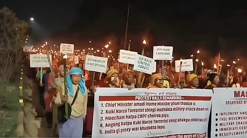 Protesters gather on a street in Imphal valley during unrest, with security forces deployed amid clashes and road blockades.