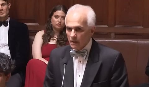 In the image Ben Habib is shown adressing the people in a podium behind him two people are shown with one girl and a man