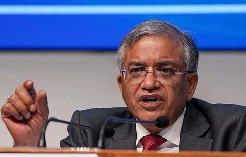 CEC Gyanesh Kumar in a suit and red tie speaks into microphones at a press conference. His expression is serious, with a backdrop of a blue screen.