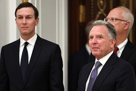 Three men in suits stand together in an elegant room, looking attentive. The atmosphere is formal with neutral expressions and focused attention.