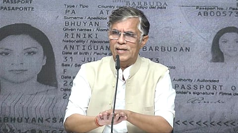 Pawan Khera sits before a mic in front of a photo of a passport of Riniki Bhuyan Sarma 