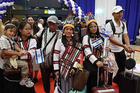 Bnei Menashe community members stand with Israeli flags in Mizo attire in front of a balloon arch