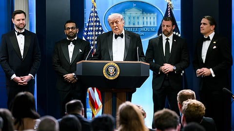 Trump stands at a podium in a tuxedo with members of his adminstration behind him