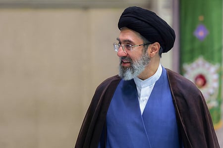 Image of supreme leader Mojtaba Khamenei looking sideways. he is wearing his glasses and background is blurred. 