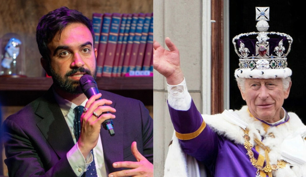 A man in a suit speaks into a microphone beside a shelf of books. To the right, a person dressed as royalty waves, wearing a purple robe and ornate crown.