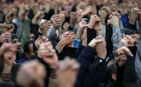 A large crowd raises clenched hands in unity, conveying solidarity. The image captures a sense of collective strength and shared purpose.