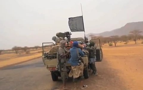 Militants gather around a pickup truck with a mounted weapon in a desert landscape. A black flag waves above, conveying urgency and unrest.
