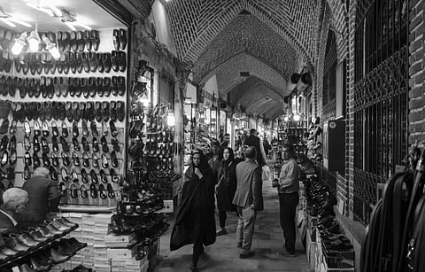 A bustling shoe market in a historical bazaar, featuring arched brick ceilings. Shelves of shoes line the walls as people browse, creating a lively atmosphere.