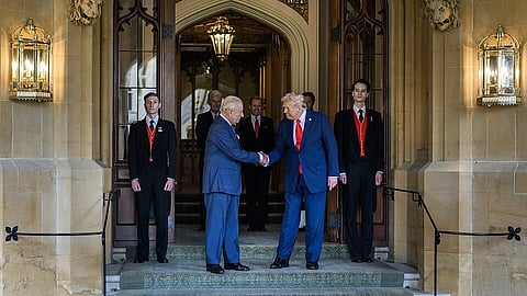 In an ornate setting, two older men in formal attire shake hands warmly on a stone entryway, flanked by serious attendants, conveying diplomacy.