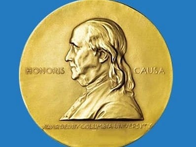 Gold Pulitzer Prize medallion featuring a side profile of Benjamin Franklin, with "Honoris Causa" text. Below, "The Pulitzer Prizes" is written in white on blue.