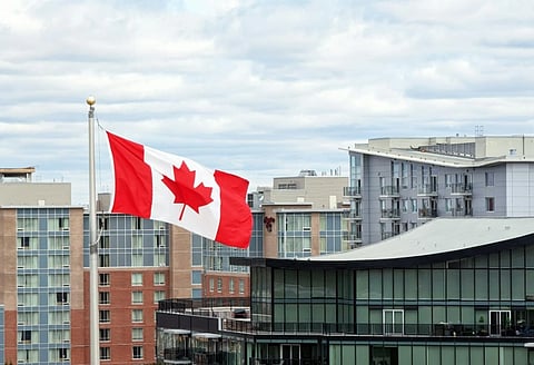 Canadian flag waving against a cloudy sky, with modern buildings in the background. The scene conveys a sense of national pride and urban life.