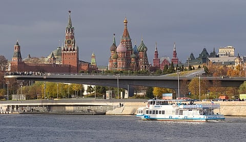 River scene with a white tour boat in the foreground. Beyond, a modern pedestrian bridge and historic buildings with colorful domes under a cloudy sky.