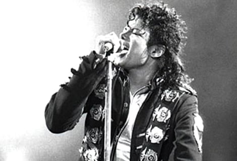 Singer passionately performing on stage, leaning into a microphone. Dressed in a decorative jacket, the scene captures intense emotion and energy.