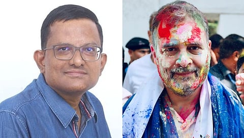 Two men side by side: the left wears glasses and a blue shirt, smiling slightly; the right is covered in bright Holi colors, smiling with festive joy.