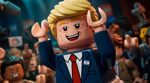 Lego character with blonde hair, wearing a suit and red tie, smiles and raises arms amidst a cheering crowd. The atmosphere is celebratory and lively.