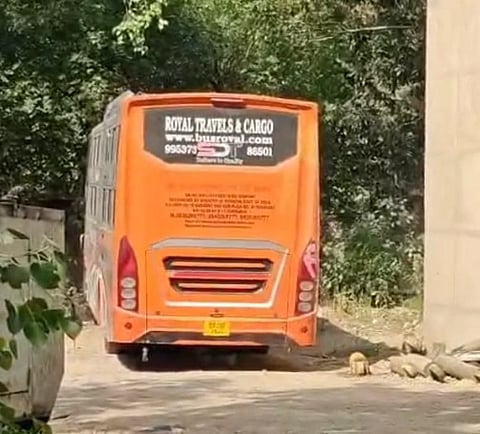 Orange bus labelled "Royal Travels & Cargo" on a narrow road, surrounded by greenery.