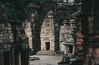 Ancient stone temple structures with intricate carvings stand under soft, dim light, evoking a sense of tranquility and historical reverence.