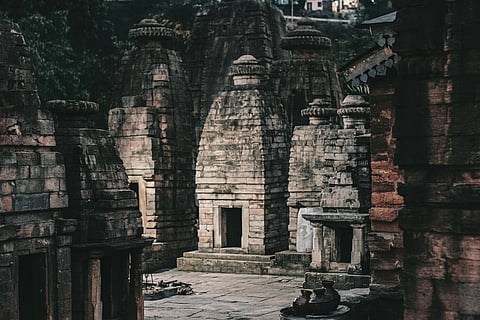 Ancient stone temple structures with intricate carvings stand under soft, dim light, evoking a sense of tranquility and historical reverence.