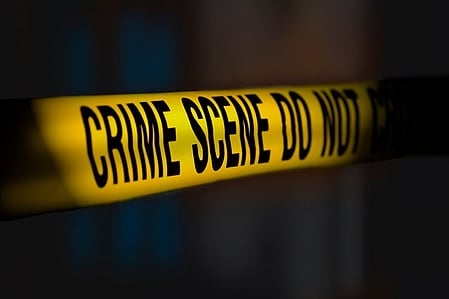 Yellow crime scene tape with bold black letters reading "Crime Scene Do Not Cross," set against a dark, shadowy background, creates a tense atmosphere.