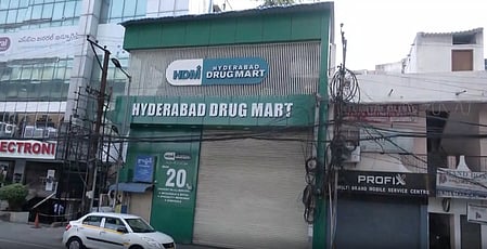 In the image a alley is shown with a big building names "Hyderabad Drug Mart"