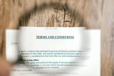 A magnifying glass focuses on the words "Terms and Conditions" on a document resting on a wooden surface, highlighting the importance of the text.