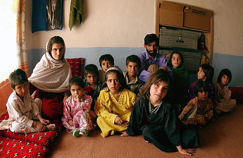 Afghan father sitting with young daughters amid poverty and humanitarian crisis in Afghanistan