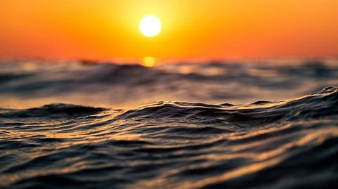 Vibrant sunset over a calm ocean with gentle waves reflecting orange and gold hues, creating a serene and peaceful atmosphere.