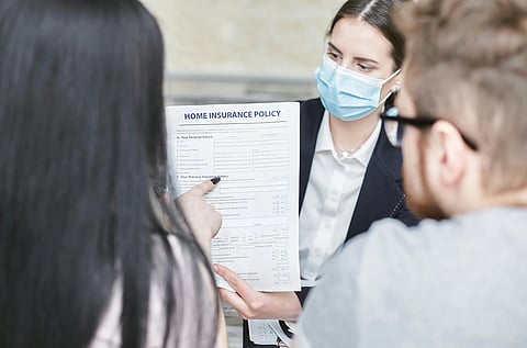 In the image a couple is shown looking at a health insurance policy form with a agent in mask showing them that