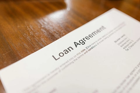 Close-up of a loan agreement document on a wooden table. The focus is on the bold title "Loan Agreement," with text details slightly blurred.