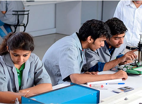 Three students in lab coats work intently at a lab table, focusing on equipment and notes. A collaborative atmosphere is depicted.
