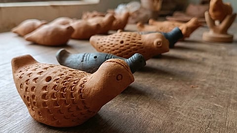 Clay bird whistles in a row on a wooden table, well-lit by a nearby window, create a rustic, artistic atmosphere. The focus is on their intricate textures.