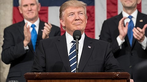 In the image Donald Trump is shown addressing the people behind him are two people Flanked by Vice President Mike Pence and Speaker of the House Paul Ryan standing and clapping for him