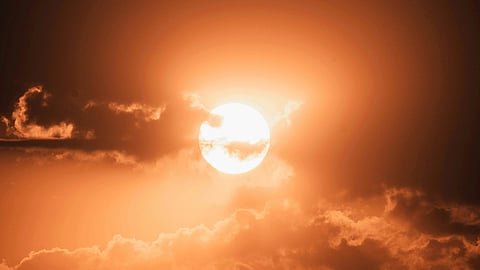 Glowing orange sun setting behind scattered clouds, casting warm light across the sky. The scene conveys a calm, serene, and peaceful ambiance.