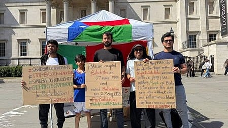 In the image four people are shown with three boards where text is written for balochistan behind them is a tent