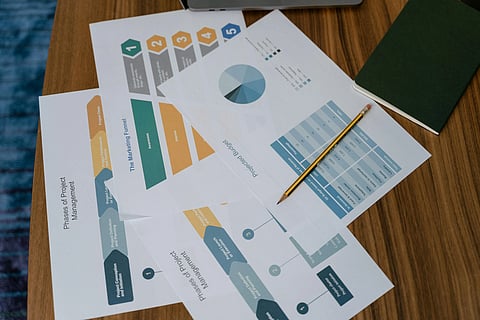 Overhead view of project management charts and graphs on a wooden table, with a pencil and a closed green notebook, conveying a professional tone