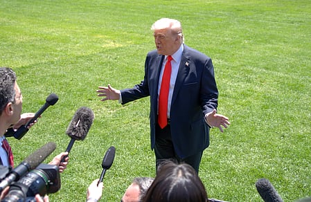 Image of Donald Trump talking to press on a green ground. 
