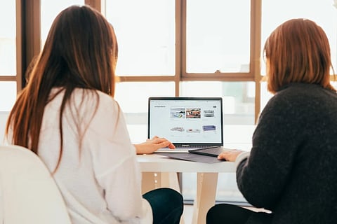 This image is showing that two women are sitting in front of laptop while discussing about productivity issues at work. 