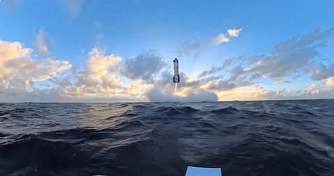 A rocket ascends against a backdrop of a bright blue sky and fluffy clouds over a vast ocean, creating a dramatic and inspiring scene.