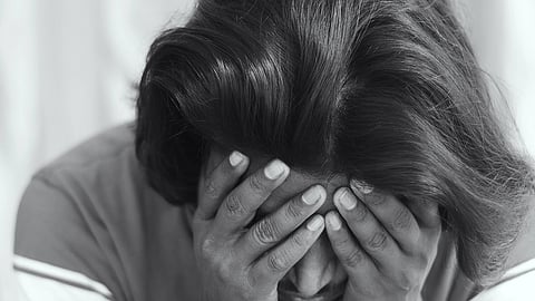 A person with shoulder-length hair, in a striped shirt, leans forward with their face buried in their hands, conveying a sense of distress or anxiety.