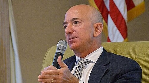 Jeff Bezos, dressed in a suit and tie, seated and engaged in conversation.