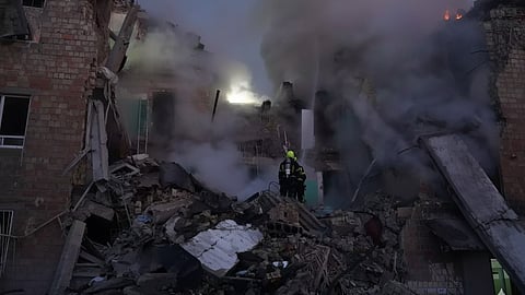 A firefighter stands before a destroyed building, highlighting the devastation from Russia's attack on Ukraine.