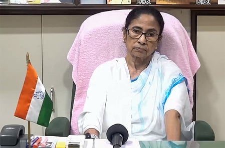 In the image Mamata Banerjee is shown sitting in a chair in which a TMC flag is shown