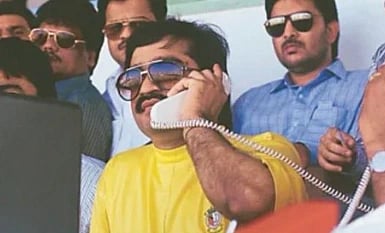 Image of young dawood ibrahim in a yellow t shirt. he is wearing sun glasses and holding a telephone. 