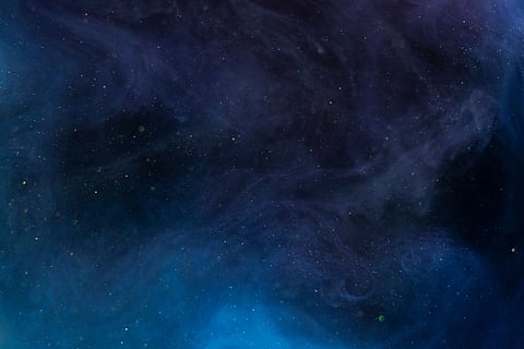 A cosmic scene of a dark, swirling nebula with deep blue and purple tones. Specks of light resemble stars, evoking a sense of mystery and wonder.
