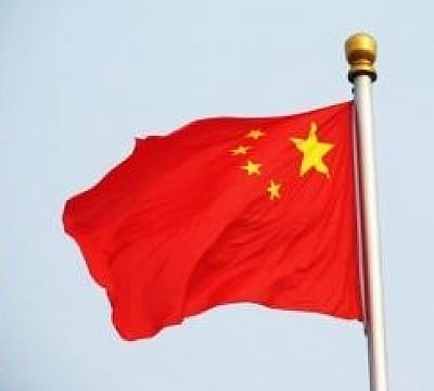 A red flag featuring one large yellow star and four smaller stars flutters against a clear blue sky. A golden pole holds the flag aloft.